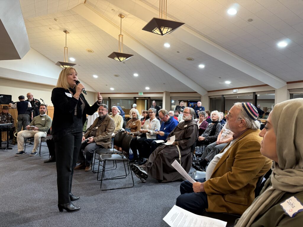 Photo of Rosemarie welcoming the audience to Friendsgiving 2024 in the Saint Joan of Arc Parish Multipurpose Room.